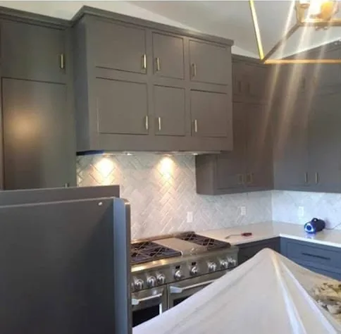 Kitchen cabinets painted charcoal gray with brass pulls over a herringbone tile backsplash