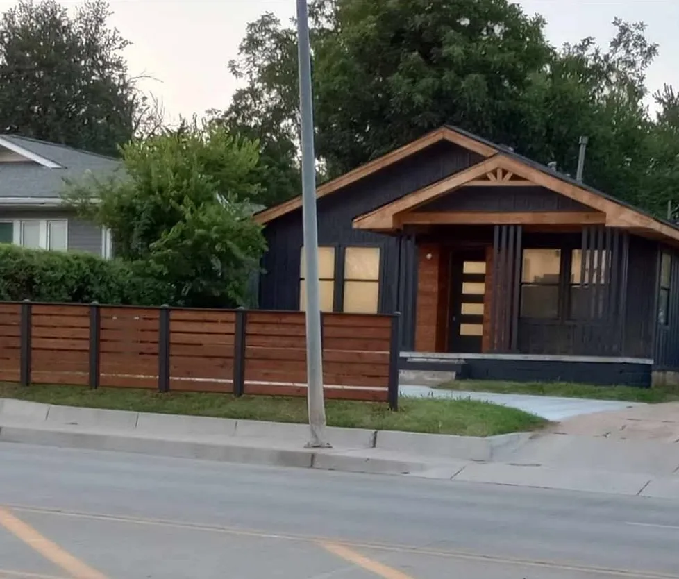 Home exterior with dark siding, custom cedar gable trim, cedar porch posts, and a horizontal cedar fence